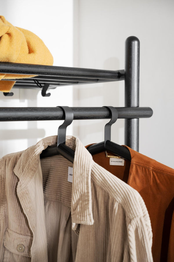 Svart klädhängare i metall med cordjackor i beige och bruna toner på vit vägg