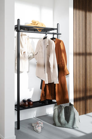 Svart klädställning i metall med hyllor, klädhängare och skor i modern hall med beige och orange kläder