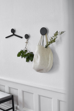Svarta väggkrokar i olika storlekar med väska och torkade blommor upphängda på vit vägg