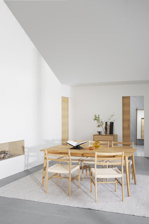 Matgrupp i ljus ek med sex stolar i minimalistiskt vardagsrum med vit vägg och grått golv