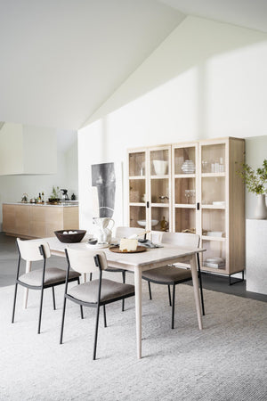 Ljus matplats med matbord i trä, stolar med grå dynor och vitrinskåp med glasdörrar i modern skandinavisk stil