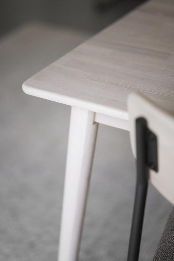 Vit träpall med rundad sits och smala ben, närbild på hörn och trästruktur