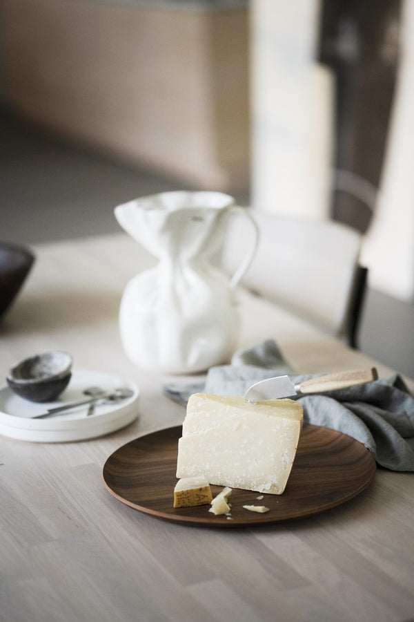 Parmesan osthyvlad på träbricka med ostkniv och grå servett i skandinavisk kökmiljö