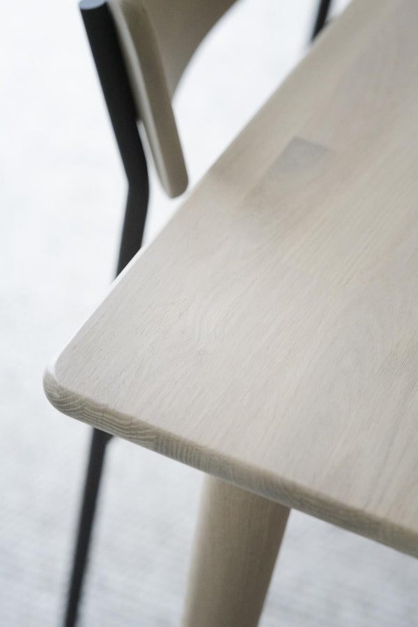 Närbild på ljus träsits med synlig trästruktur och svarta metallben på stol