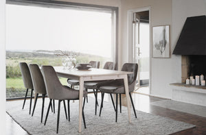 Matgrupp med ljust bord och grå sammetsstolar i modern matsal med utsikt över natur