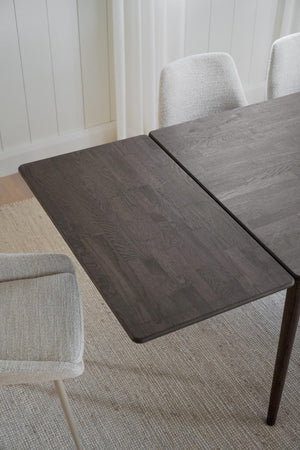 Grått matbord med utdragbar skiva i trä, omgivet av ljusgrå stoppade stolar i modern matsal