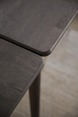 Närbild på mörkbrun träbordsskiva med rundade hörn och synlig trästruktur