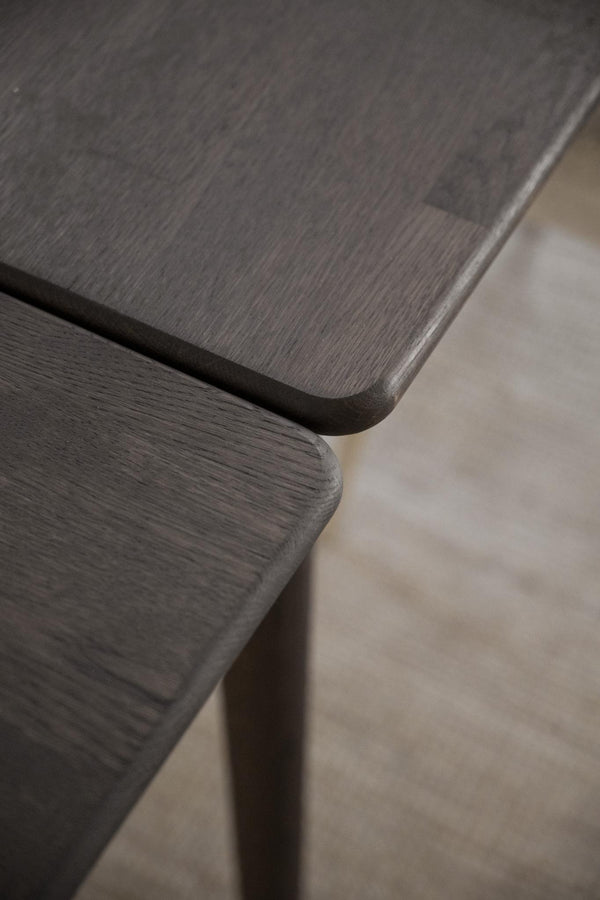 Närbild på mörkbrun träbordsskiva med rundade hörn och synlig trästruktur