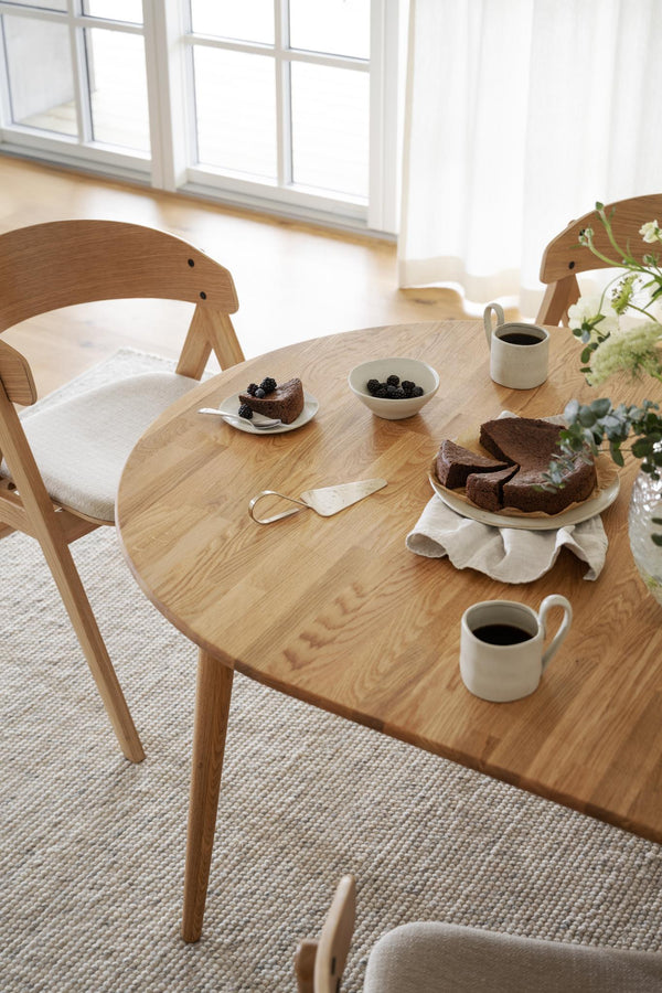 Runt matbord i ek med stolar och chokladkaka, kaffekoppar och blåbär i ljust skandinaviskt kök
