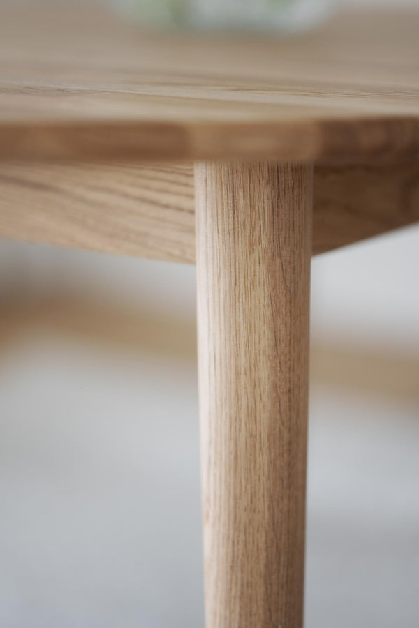 Närbild på ljust träbord med synlig trästruktur och ben i massiv ek
