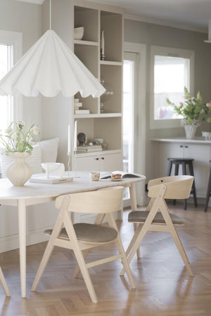 Ljus matplats med vit taklampa, runt matbord och ljusa trästolar i skandinavisk stil