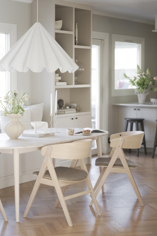 Ljus matplats med vit taklampa, runt matbord och ljusa trästolar i skandinavisk stil