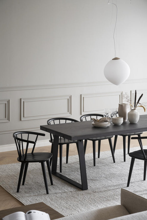 Svart matbord med matchande stolar i modern skandinavisk stil, vit taklampa och ljus väggpanel i matsal