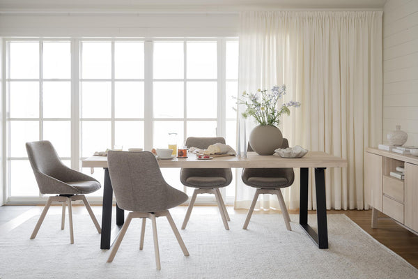 Modern matgrupp med ljust trä och grå stolar vid fönster med vita gardiner