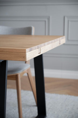 Matbord i ljust trä med svarta ben och modern design, närbild på hörn med synlig snickeridetaj