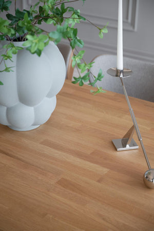 Modern bordslampa i silver på träbord bredvid vit skulpturell vas med grön växt