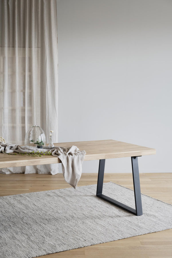 Matbord i ljust trä med svarta metallben på ljusgrå matta i minimalistisk skandinavisk stil