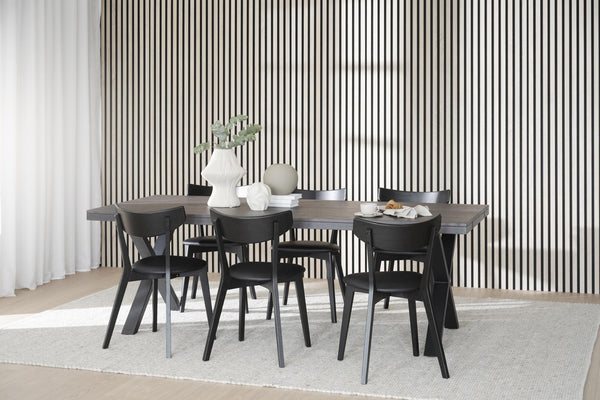 Matbord i grått trä med sex svarta stolar i modern skandinavisk stil mot randig vägg