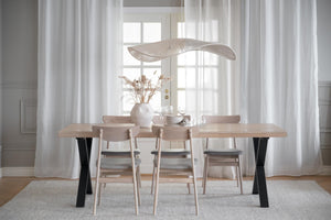 Matbord i ljust trä med svarta ben och matchande stolar i skandinavisk stil, uppdukad matplats med gardiner