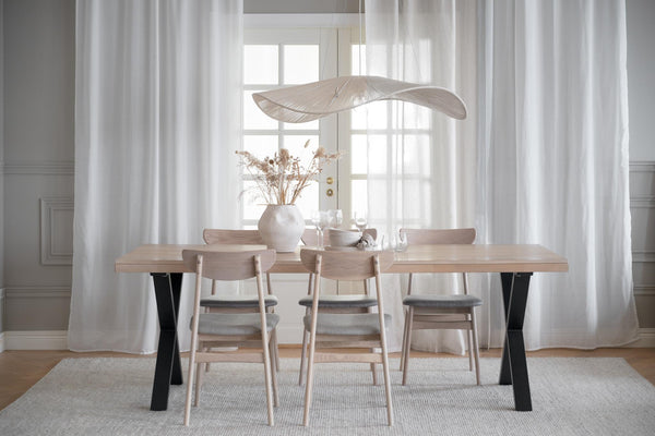 Matbord i ljust trä med svarta ben och matchande stolar i skandinavisk stil, uppdukad matplats med gardiner