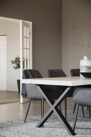 Matbord med ljus träskiva och svart kryss-stativ omgivet av grå och svarta stolar i modern matsal