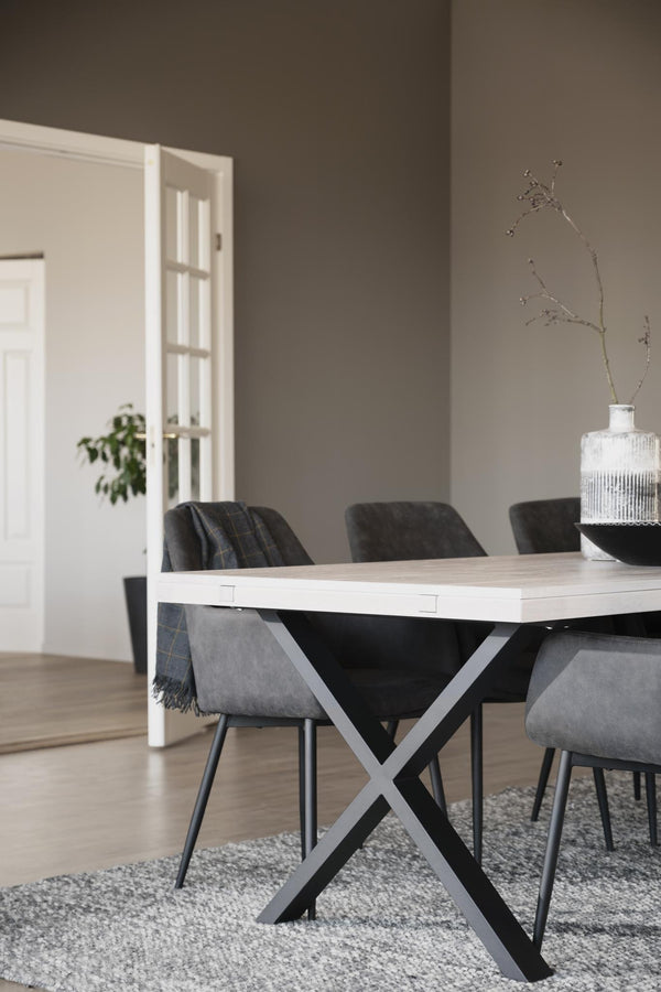 Matbord med ljus träskiva och svart kryss-stativ omgivet av grå och svarta stolar i modern matsal