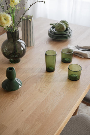 Gröna glasvaser och dricksglas på träbord med blommor i skandinavisk inredningsstil