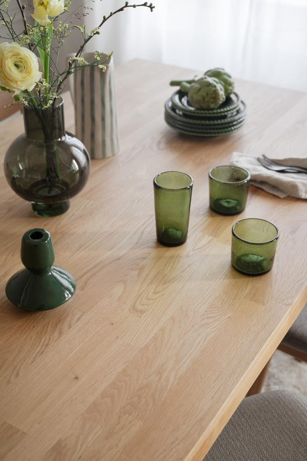 Gröna glasvaser och dricksglas på träbord med blommor i skandinavisk inredningsstil