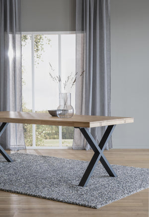 Matbord i ljust trä med svarta kryss-ben på grå matta framför fönster med vita gardiner