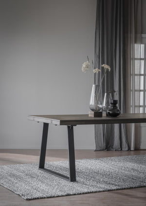 Matbord med uttragsfunktion i mörkt trä och svarta ben, dekorerat med vaser på rund matta i grått rum