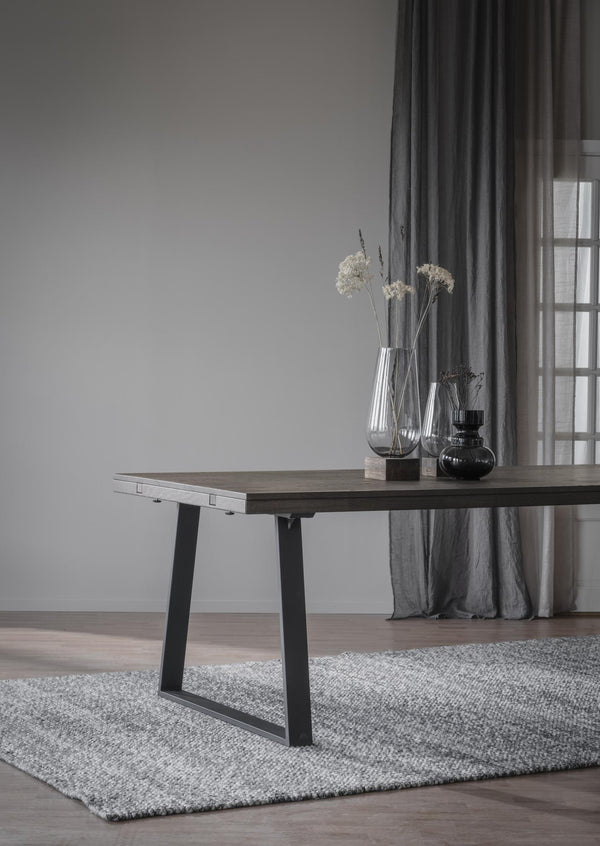 Matbord med uttragsfunktion i mörkt trä och svarta ben, dekorerat med vaser på rund matta i grått rum