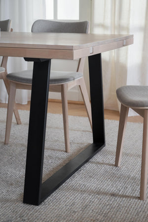 Matbord med ljust trä och svarta metallben tillsammans med grå stoppade stolar på ljus matta