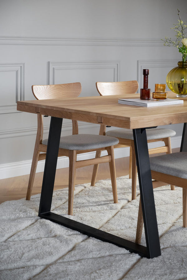 Matbord i ek med svarta metallben och stolar med grå klädsel på vit matta i ljust rum