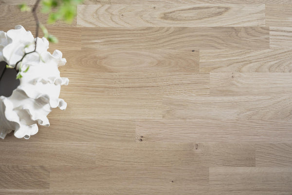 Ljust trägolv i ek med naturlig struktur och vit orkidé i kruka
