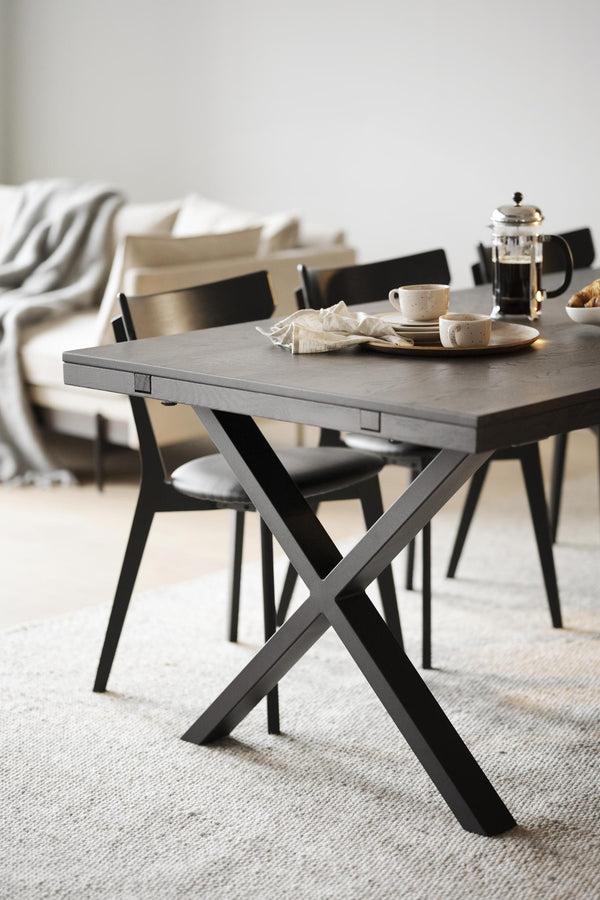 Matbord med grå skiva och svarta korsben, omgivet av svarta stolar i modern skandinavisk stil