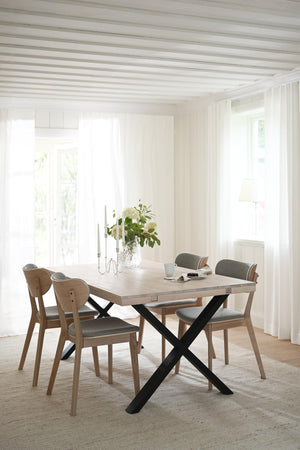 Matbord med krysskena i ljust trä och svart metall, omgivet av stolar med grå stoppad sits i ljust matrum