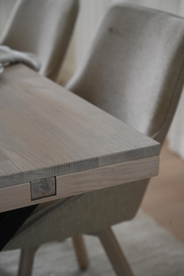 Matbord i ljust trä med synlig trästruktur och grå stopperade stolar i bakgrunden