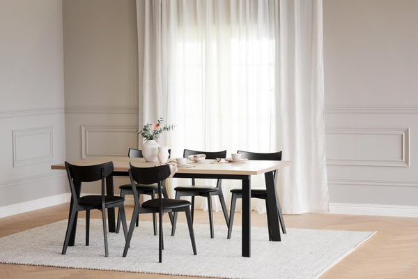 Matgrupp med ljust träbord och svarta stolar i modern matsal med vita gardiner