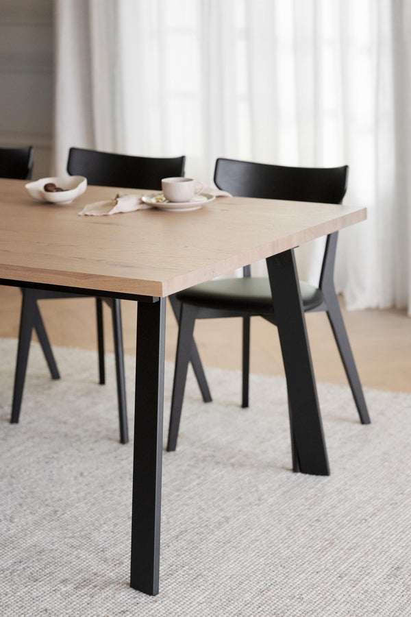 Matbord i ljust trä med svarta ben och matchande svarta stolar i modern skandinavisk design