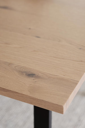 Bordsskiva i ljus ek med synliga årsringar och naturliga kvistar, monterad på svart stativ