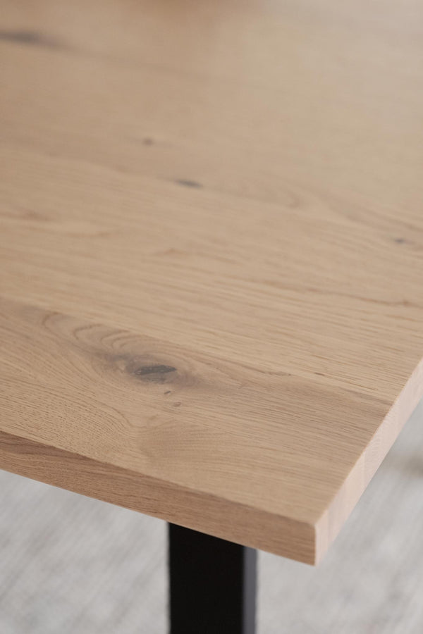 Bordsskiva i ljus ek med synliga årsringar och naturliga kvistar, monterad på svart stativ