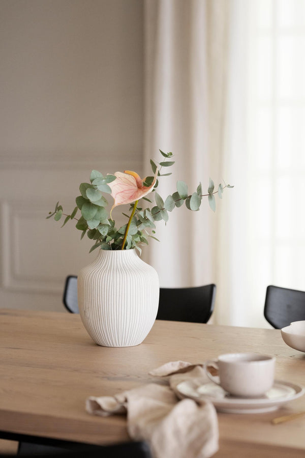 Vit räfflad vas med eucalyptus och rosa blomma på matbord i ljust skandinaviskt kök