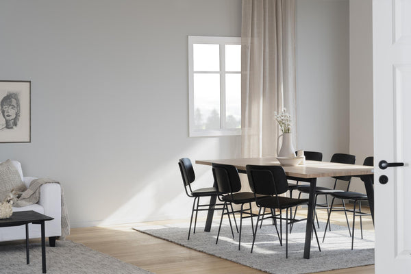 Matbord i ljust trä med svarta stolar i minimalistisk matsal med beige gardiner och ljusinsläpp
