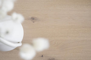 Vit keramisk vas med torkade blommor på ljust trägolv i skandinavisk stil