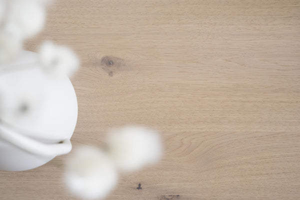 Vit keramisk vas med torkade blommor på ljust trägolv i skandinavisk stil