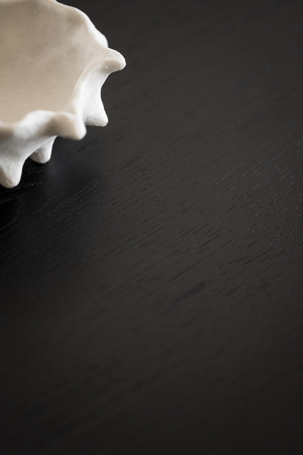 Vit keramikskål med vågad kant på mörk träyta, närbild av dekorativ serveringsskål