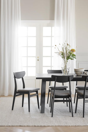 Matgrupp med svarta stolar och bord i skandinavisk stil med blomvas som dekoration i ljust matrum