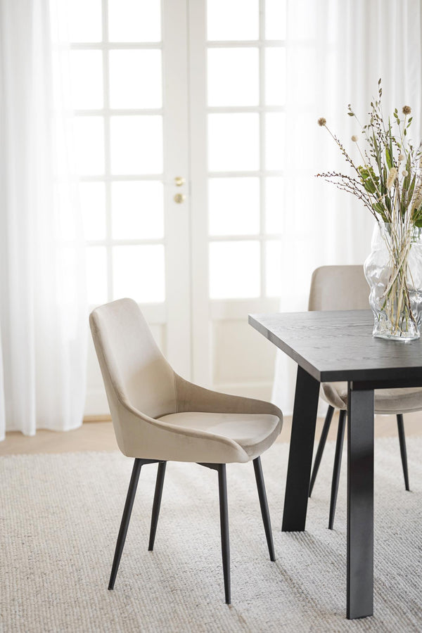 Beige matstol med svarta ben vid matbord i modern skandinavisk matsal med ljusinsläpp