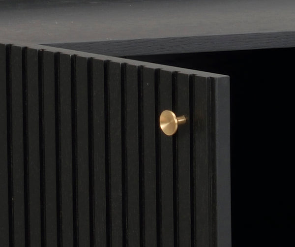 Svart skänk med räfflad front och gyllene rund knapp i mässing, närbildsdetalj av luckhandtag