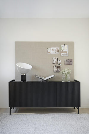 Svart skänk med räfflad front och moodboard med inspirationsbilder, lampa och vas med blommor